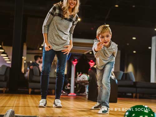 Mom and son throwing bowling ball down the lane.