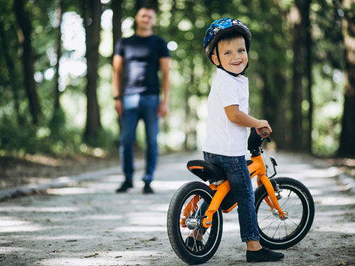 Man teaching young son how to ride a bicycle on a paved, tree-lined trail in Branson.