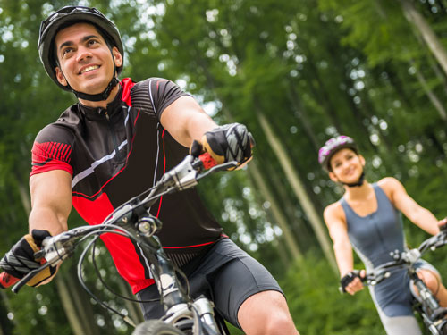 Man and woman wearing helmets and riding bicycles on a tree-lined trail in Branson.