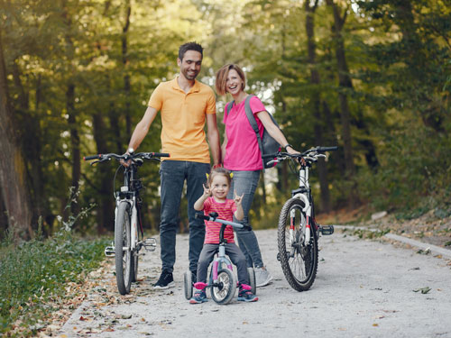 Family of three biking on a nature trail in Branson. Young daughter with pigtails is throwing up peace signs with her hands and is the main focus.