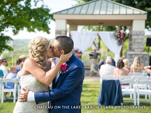 Newlywed couple kissing at the end of the aisle after their outdoor wedding ceremony.
