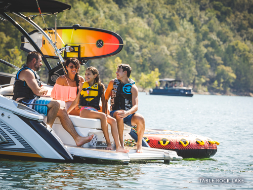 Family of four sitting on the back of a boat during summer, enjoying the Ozark Mountain scenery on a lake in Branson.
