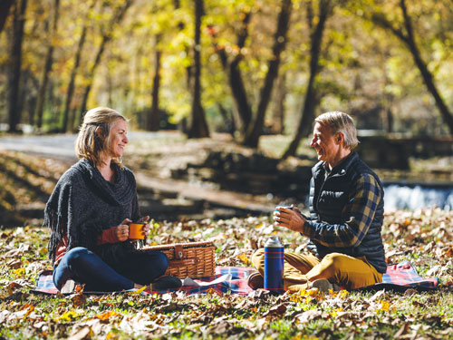 Middle-aged couple sitting on a picnic blanket and eating a picnic at a nature park in Branson.