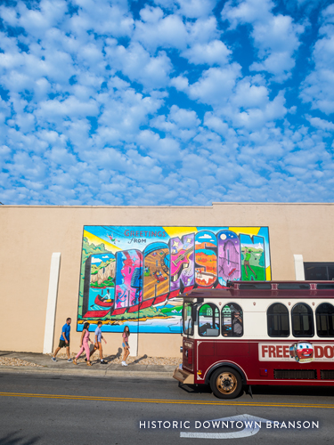 Family walking in front of Historic Downtown Branson mural wall as the free trolley passes.