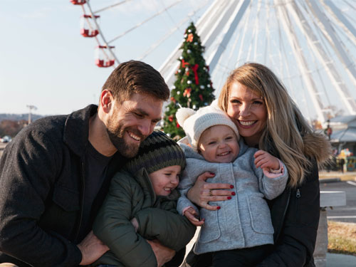 Mom and dad holding their son and daughter in front of a large Christmas tree and the Branson Ferris Wheel.