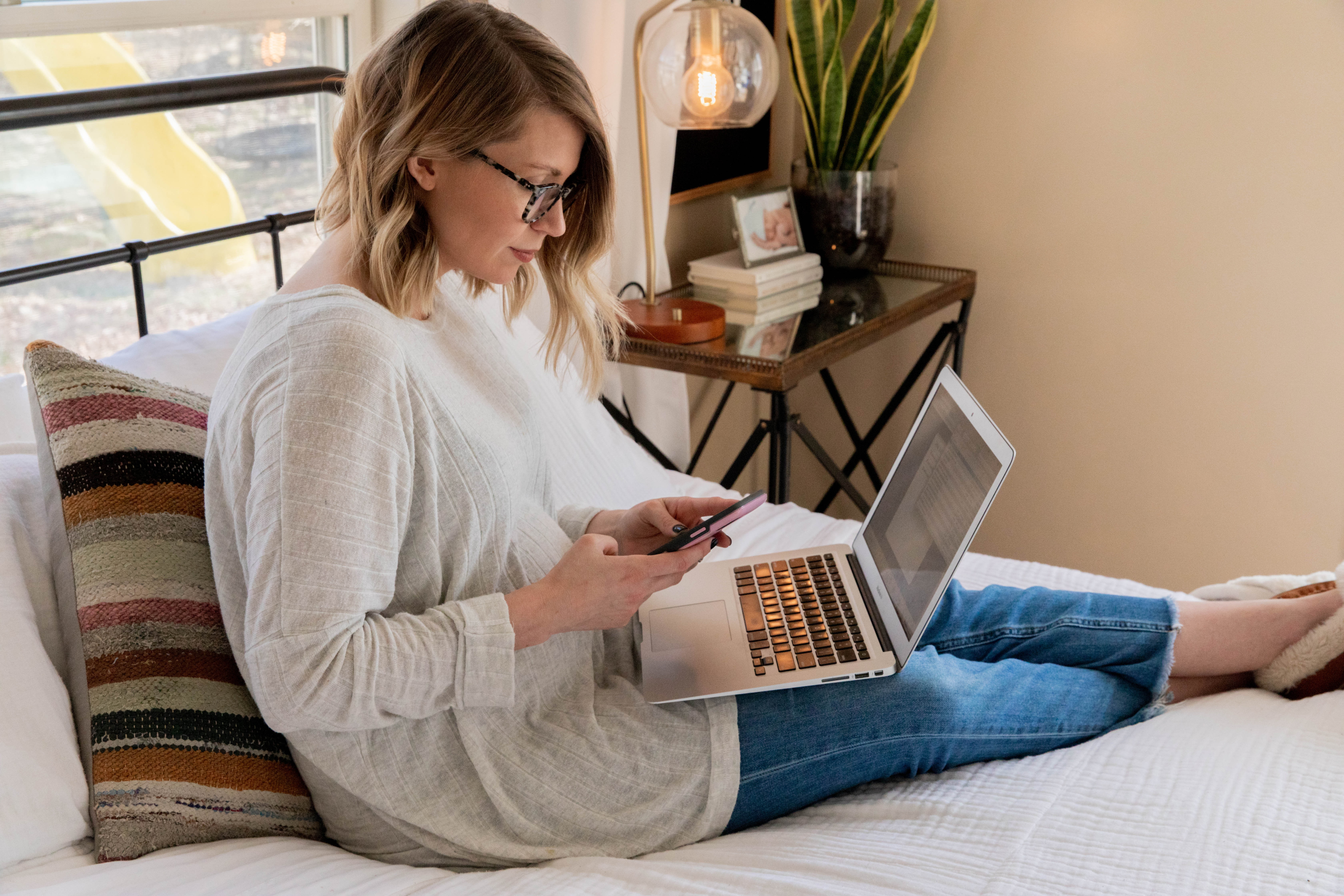 Woman sitting on bed and working on computer/phone at her home in Branson.