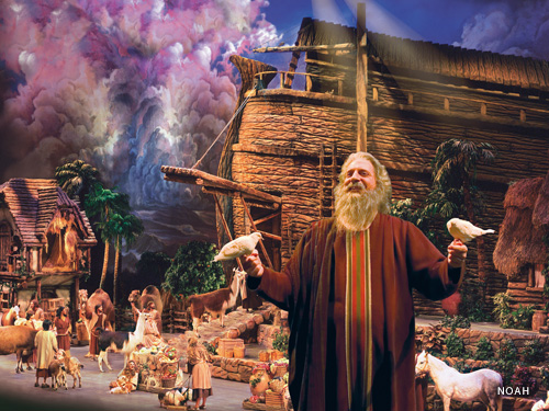 Man dressed up as a bible character is surrounded by birds and animals on a live show stage featuring an Ark in Branson.