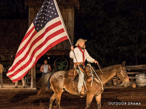 Man on horse holding a large American flag and performing in an outdoor drama in Branson.