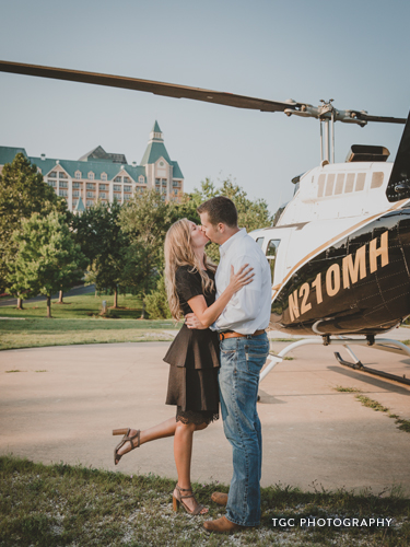 Recently engaged couple kissing in front of a helicopter.