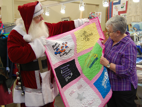 Santa showing a woman shopper a quilt in a quilt store.