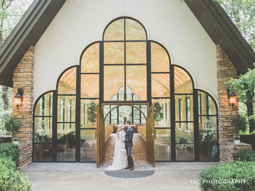 Recently married couple standing in front of a glass chapel in the Ozarks.
