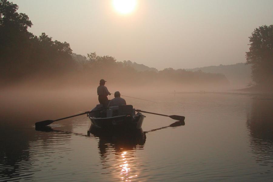 Two fishermen in a rowboat surrounded by morning mist