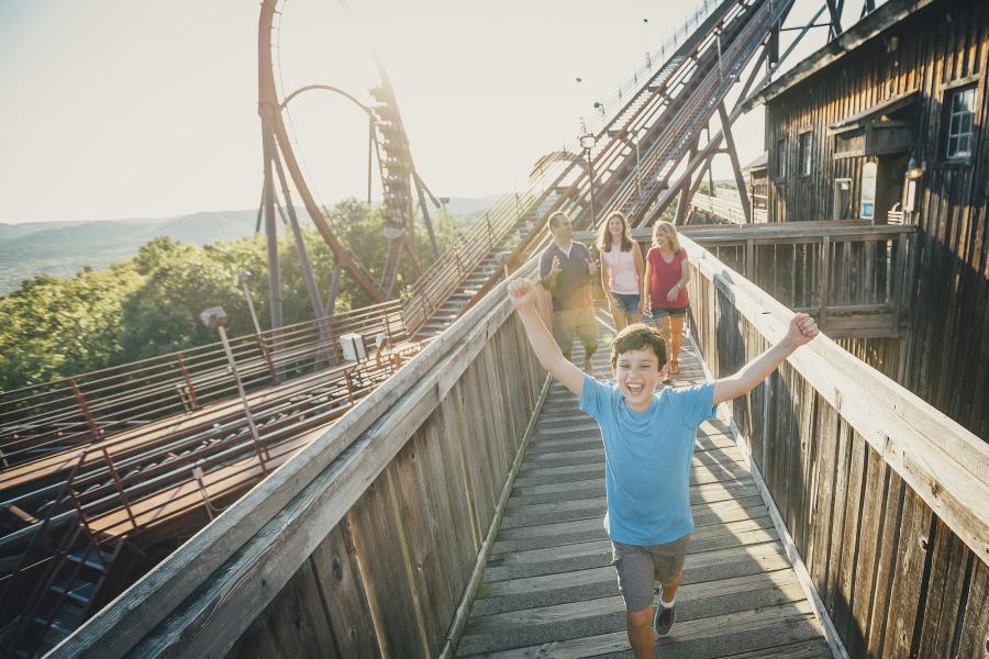 Kid running happily along with a roller coaster in the background.