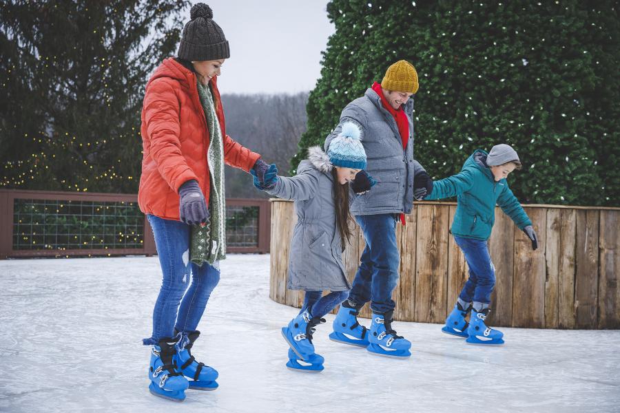 Young family of four ice skating with holiday lights in the background.