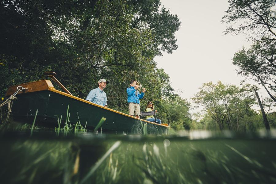 Family of three watching young son fishing off a small boat in a lake.