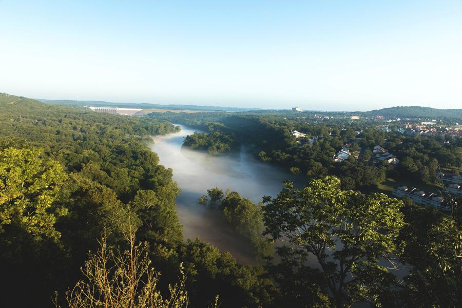 Aerial shot of fog setting in over a lake surrounded by forests and a town