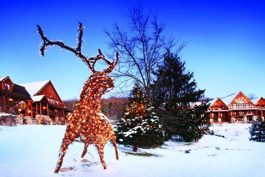 Reindeer made out of wood and string lights standing in front of Big Cedar Lodge cabins on snow-covered ground.