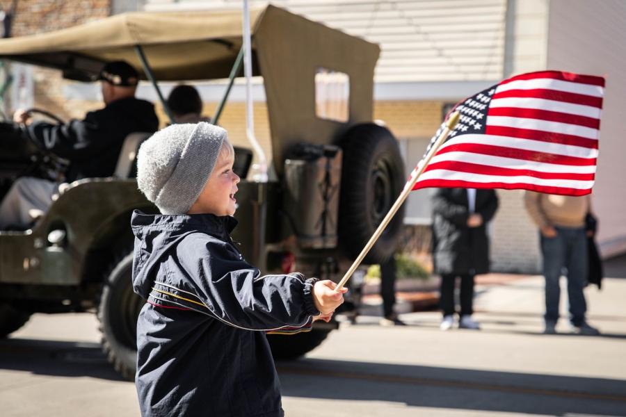 little boy waves flag in front of military jeep at veterans day parade in branson mo