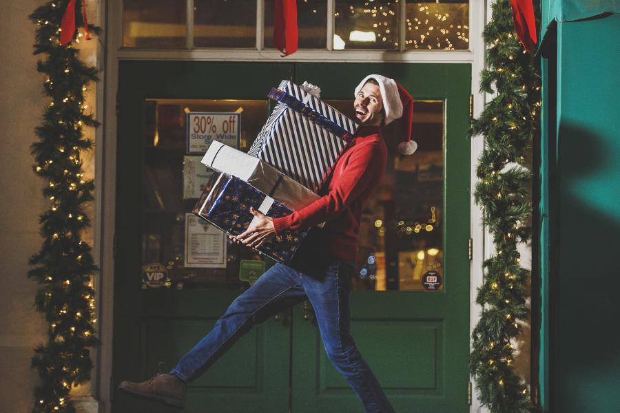 guy holding christmas boxes smiling in front of store