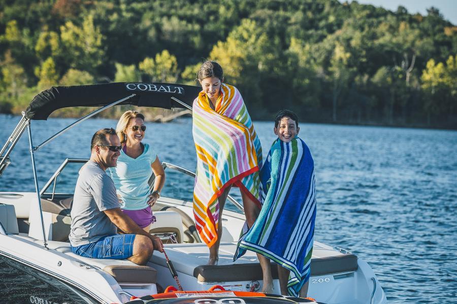 two parents sit on their boat on table rock lake watching their song and daughter dry off with towels