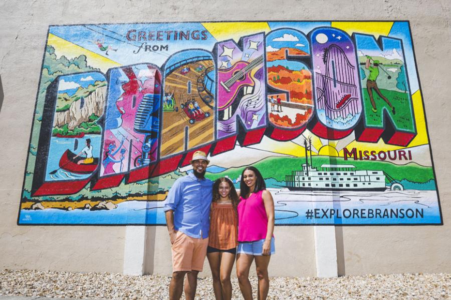 Husband, wife and daughter pose in front of a colorful mural in Downtown Branson. 