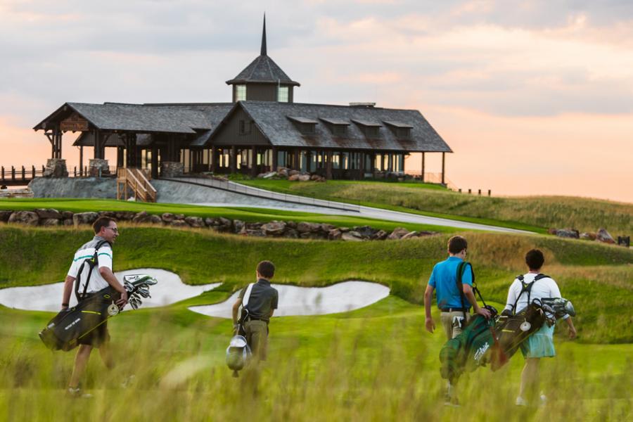 Group of four golfers walking toward clubhouse during sunset. 