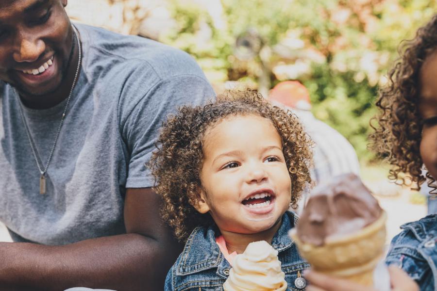 Two young girls holding ice cream cones and sitting next to their dad at a theme park in Branson.
