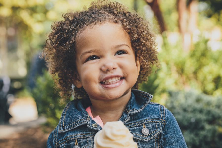 Young girl with black curly hair posing with a vanilla ice cream cone at a theme park in Branson.