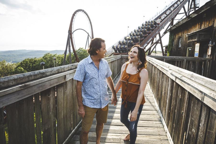 Couple holding hands and walking in front of a roller coaster ride at Silver Dollar City theme park in Branson.