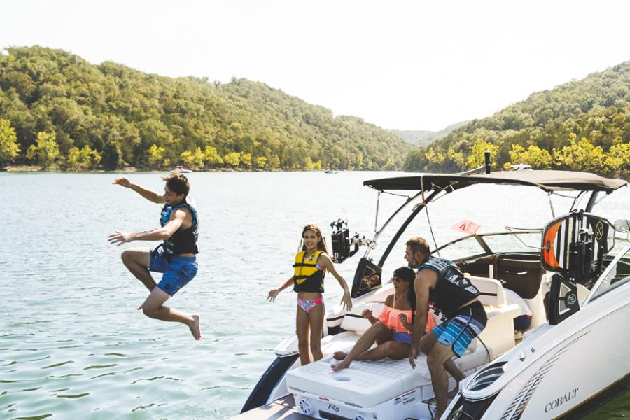 Family of four jumping off back of boat at a scenic lake in Branson.