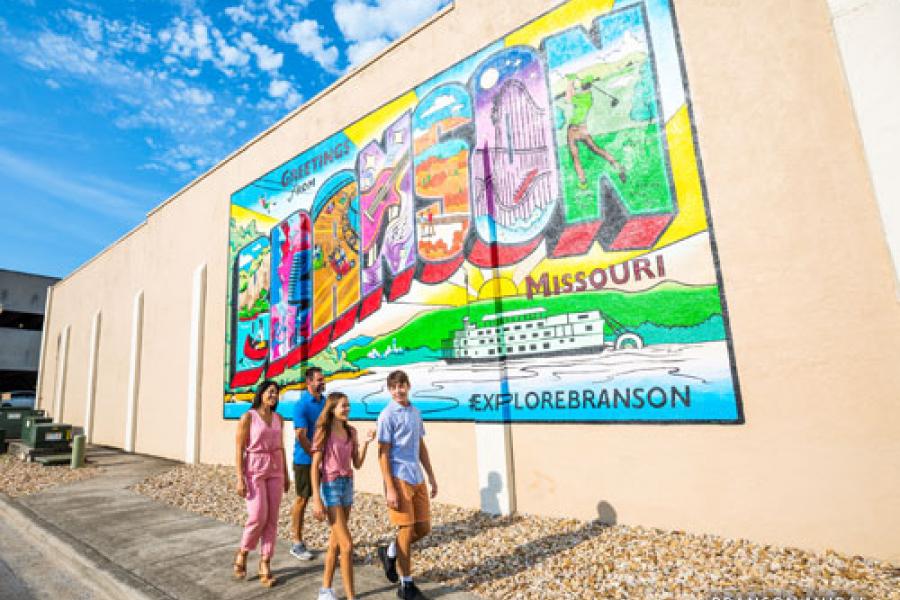Family of four walking in front of color Downtown Branson mural.