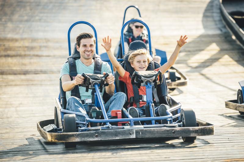 Father and son riding in a go kart with sons arms raised in the air.