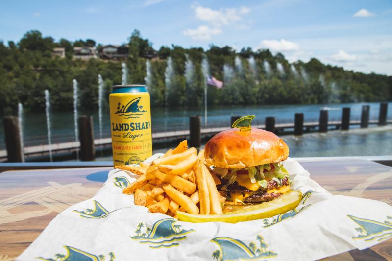 French fries and a burger on a plate with a beer overlooking the fountains at Branson Landing.