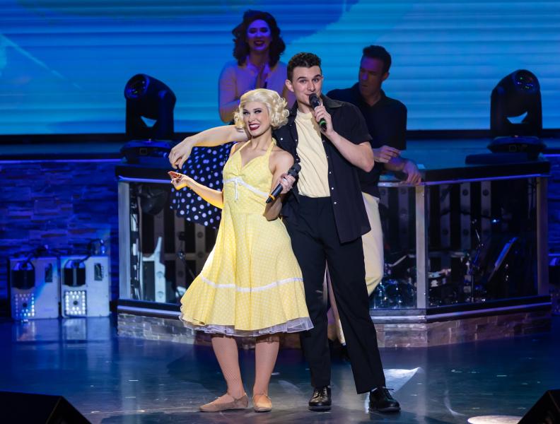 A couple sings on stage dressed in retro costumes