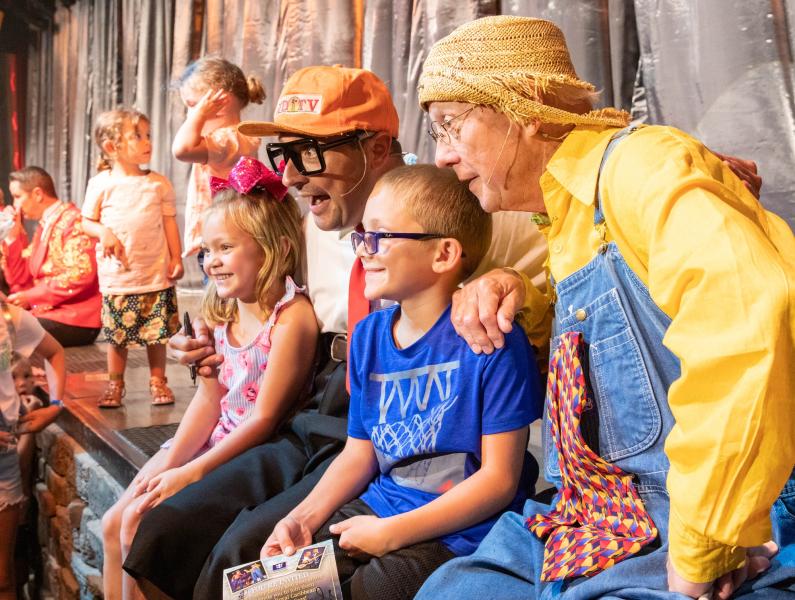 A young boy and girl meet the cast of the Presleys and are taking a picture on stage with two of the performers