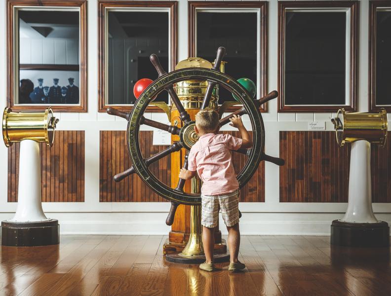 A boy plays with a wooden ship wheel