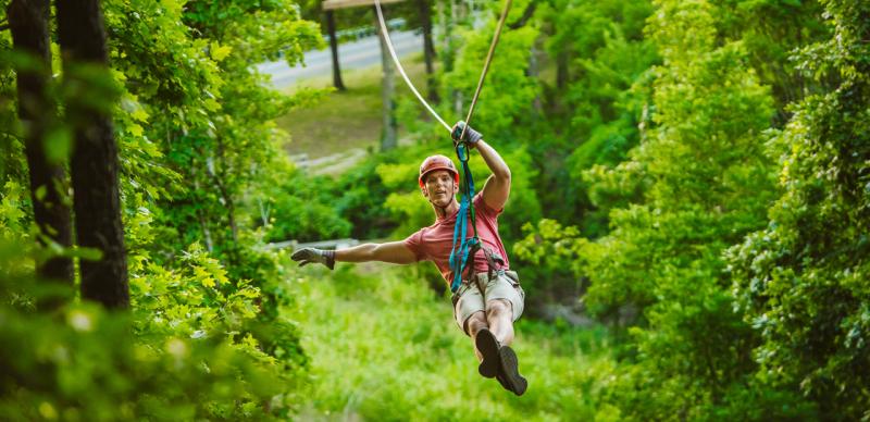 Man traveling on zipline through a forest of trees in Branson.
