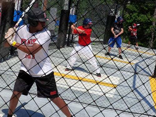 Young boys swinging a baseball bat in a Branson batting cage.