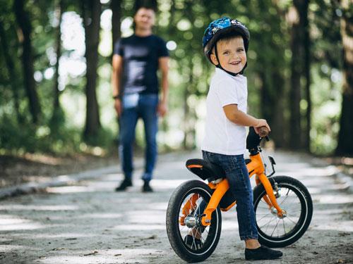 Man teaching young son how to ride a bicycle on a paved, tree-lined trail in Branson.