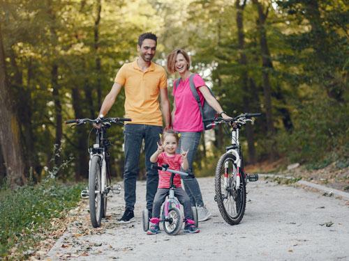 Family of three biking on a nature trail in Branson. Young daughter with pigtails is throwing up peace signs with her hands and is the main focus.