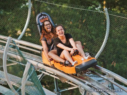 Two girls riding inside a mountain coaster car on a track in Branson.