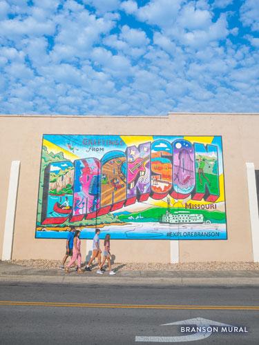 Family of four walking in front of a colorful Downtown Branson mural.