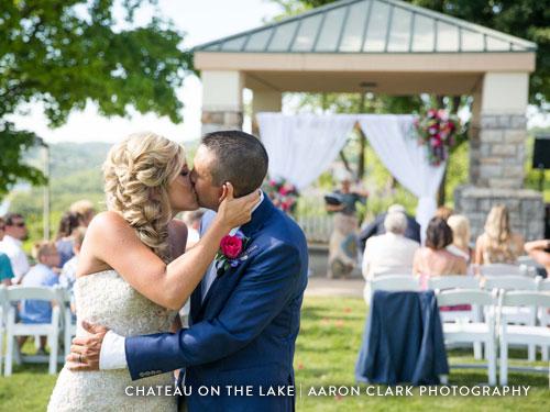 Newlywed couple kissing at the end of the aisle after their outdoor wedding ceremony.