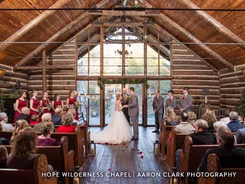Couple going through wedding ceremony with huge glass windows as a backdrop in the chapel.