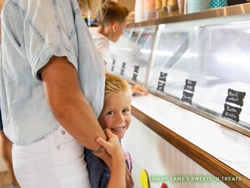 Little blonde headed boy smiling while looking at ice cream with his family.