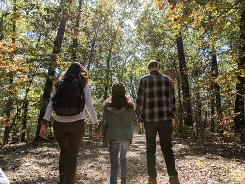 Father, mother and daughter holding hands and walking on wooded hiking trail in Branson.