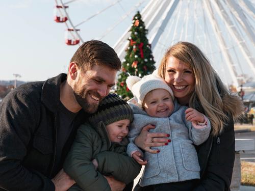 family of four enjoying a winter walk in front of ferris wheel and giant Christmas tree in Branson. 