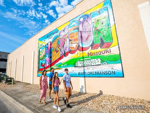 Family of four walking in front of color Downtown Branson mural.