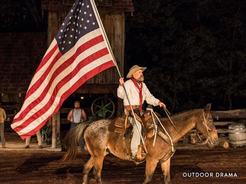 Man on horse holding a large American flag and performing in an outdoor drama in Branson.