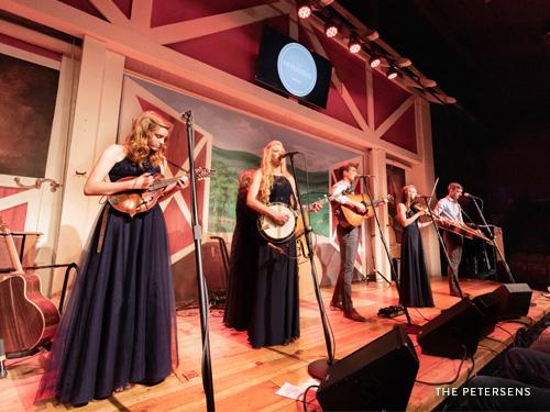 Petersen family of six playing their bluegrass instruments on stage.